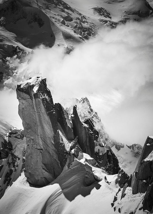 À climber at the foot of a huge pillar of rock at the Arete des Cosmiques in the Mont Blanc massif while clouds swirl around