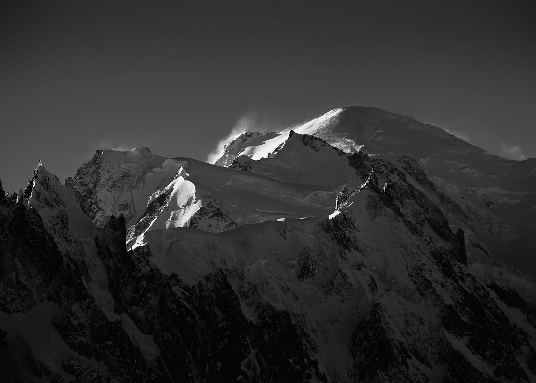Black and white photo of wind blowing snow from the summit of Mont blanc and surrounding alpine mountains