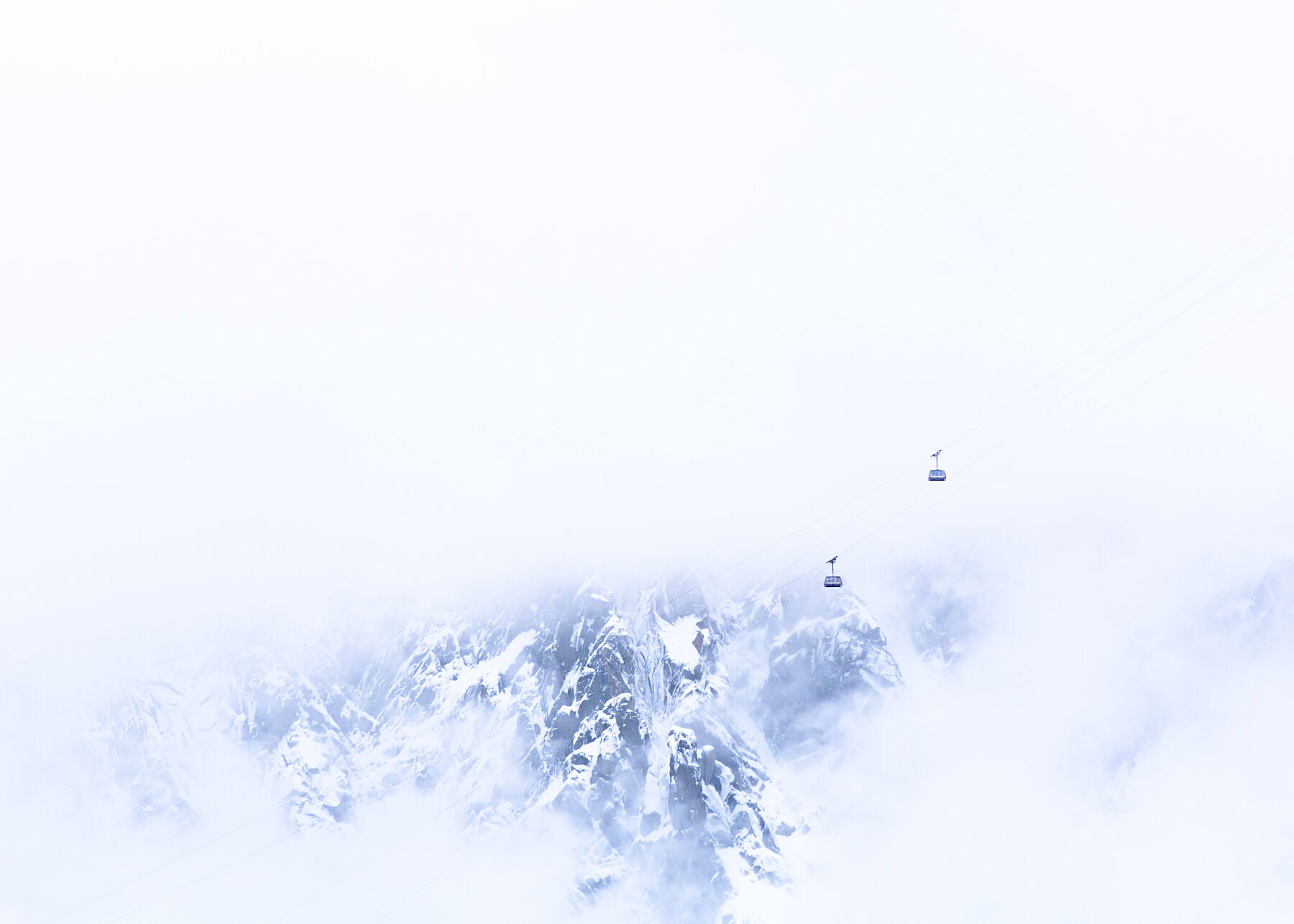 minimalist view of the Aiguille du Midi cable cars suspended in front of the rock face above Chamonix, a unique photograph that uses white space to convey the scale and beauty of the scene.