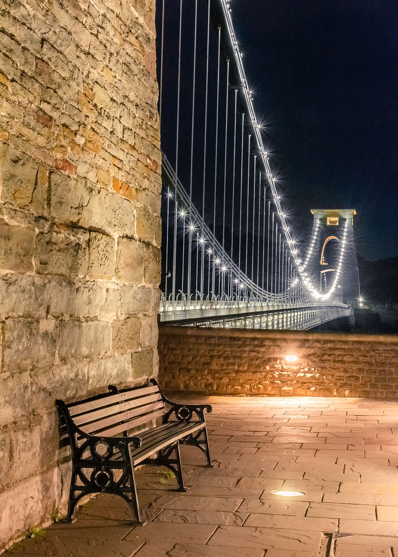 Clifton suspension bridge in Bristol at night with with a foreground seat and sparkling lights on the bridge