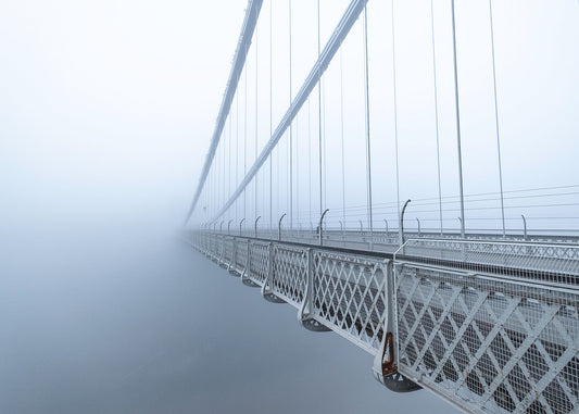 Beautiful photo of Clifton Suspension Bridge receding into thick fog as light breaks through in the distance