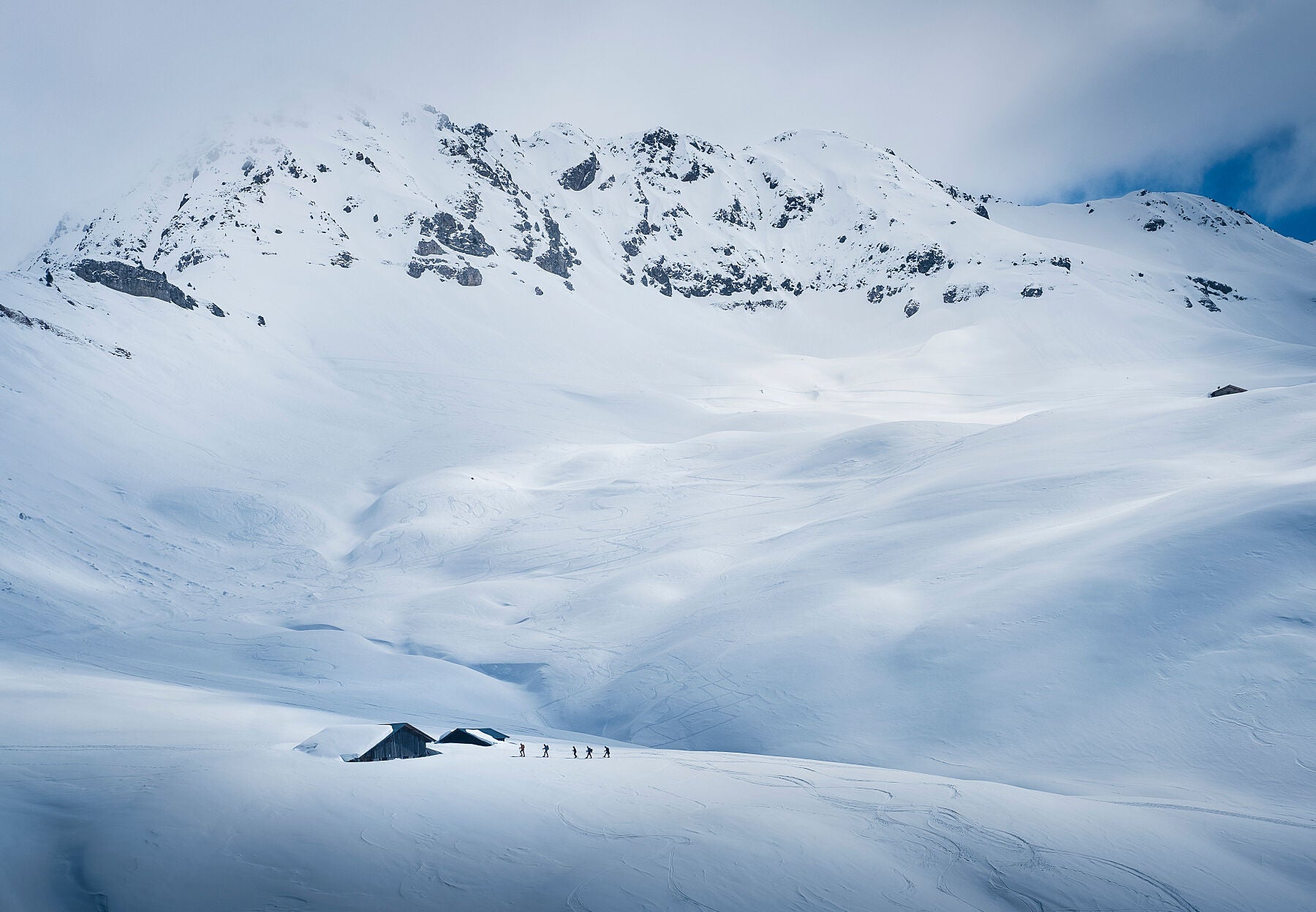 5 ski tourers arrive at a snow covered hut deep in the backcountry with a backdrop of the mountains in the Mont Blanc Massif  near Les Contamines