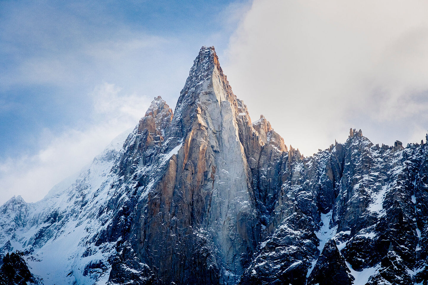 The distinctive Les Dru in the Mont Blanc Massif above chamonix, with snow covering the slopes and golden sunlight on the mountain