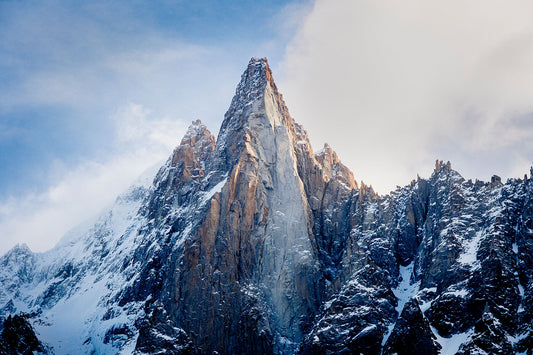 The distinctive Les Dru in the Mont Blanc Massif above chamonix, with snow covering the slopes and golden sunlight on the mountain