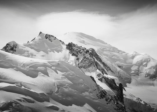 A stunning high resolution black and white photograph of summit of Mont Blanc capped by a lenticular cloud, emerging from behind the summit of the foreground Mt Tacul and glacial landscape of the Mont Blanc Massif.