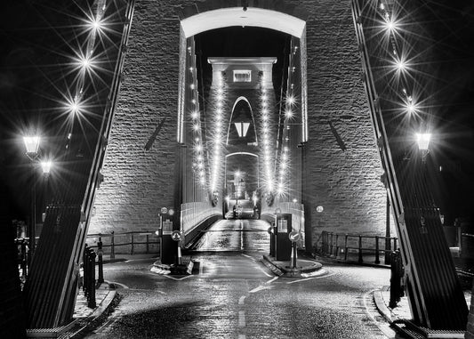 Unusual and dramatic black and white fine art photograph of Brunel’s Clifton suspension bridge in central Bristol at night  with light reflections on the wet tarmac