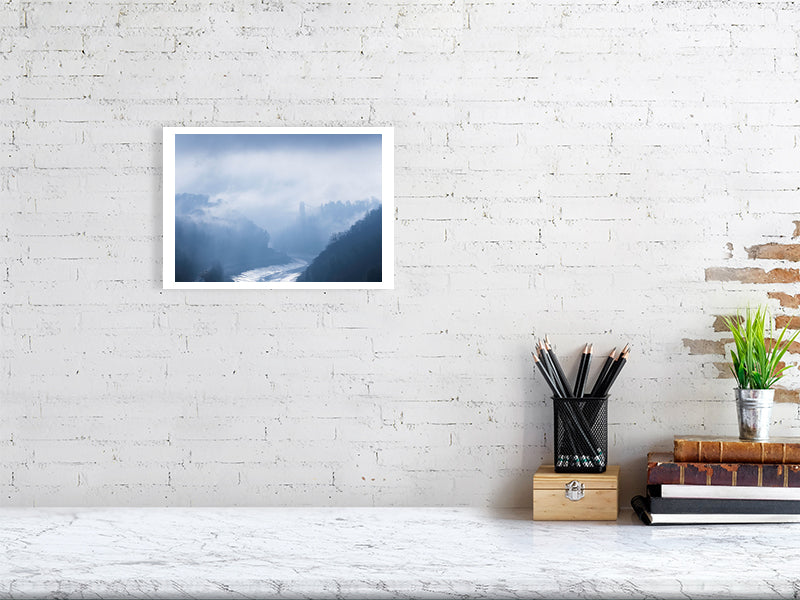 A white brick wall with a hanging picture of Clifton Suspension Bridge in the distance breaking free of the morning fog, with the River Avon below and the Avon gorge