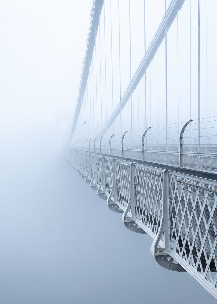Clifton Suspension Bridge in Bristol disappearing into thick mist, with suspension cables and metal railings fading into the fog.