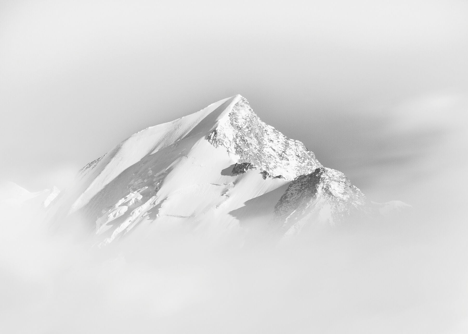 Dramatic black and white photograph of a  snowy mountain peak surrounded by cloud