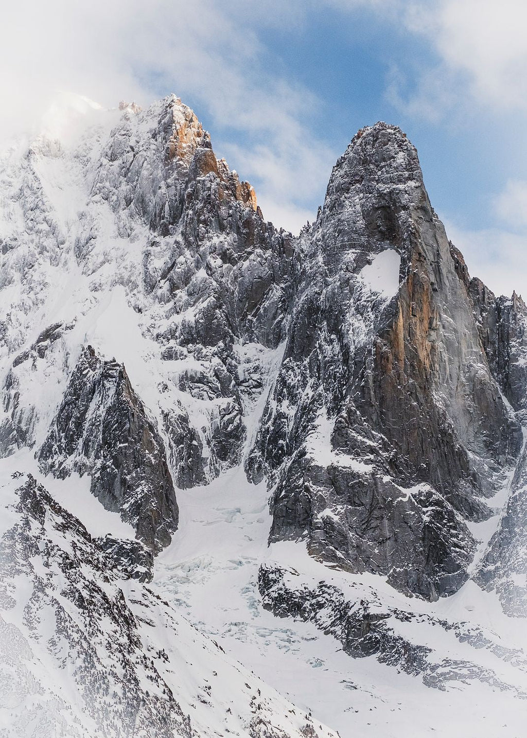 Snow encrusts the face of Les Drus, Mont Blanc Massif while in contrast the sun lights the rock face backed with a blue sky