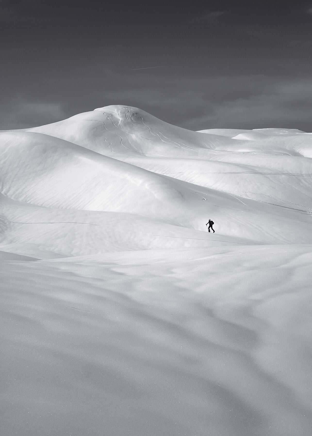 Minimalist Black and white photograph of a lone ski tourer in a field of snow with beautiful contours and lighting