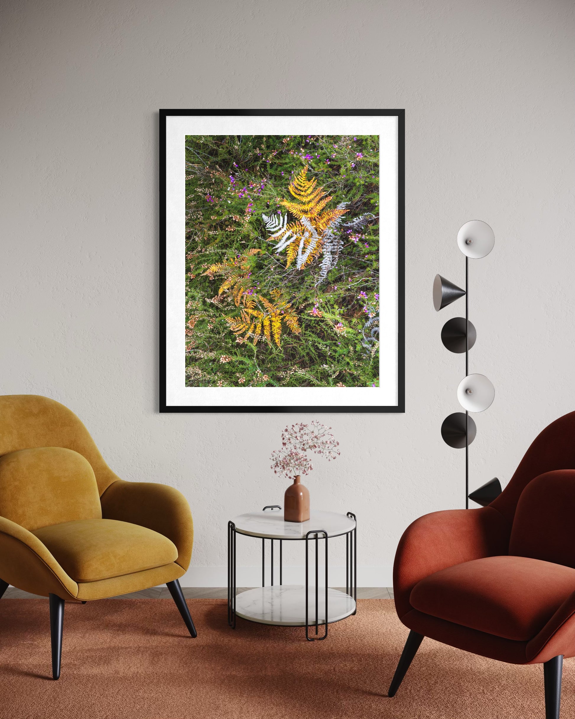A room view of a stunning photograph in a simple black frame, capturing golden autumn  leaves lying on a a green mossy ground,  creating a beautiful natural collage symbolic of the changing season. 