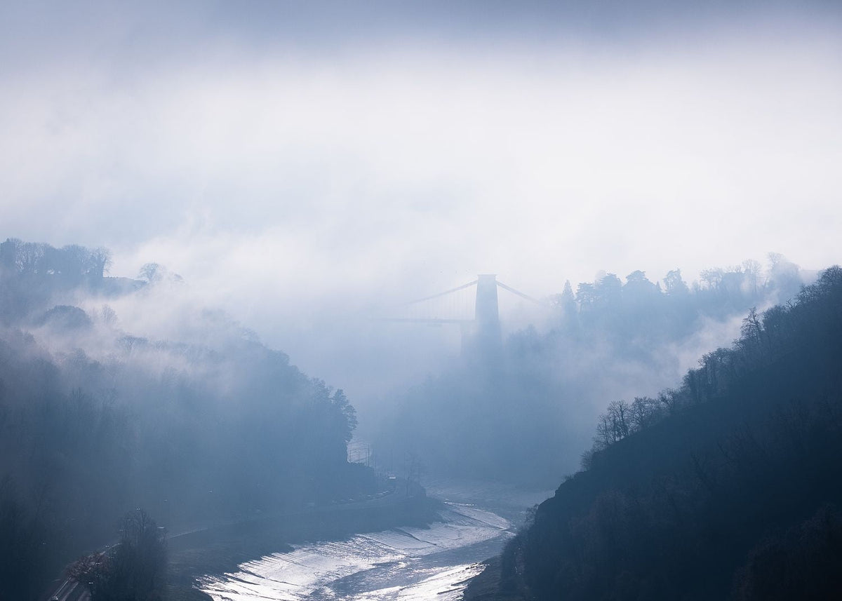 Clifton Suspension Bridge partly hidden by fog above the River Avon, with wooded slopes in Bristol’s Avon Gorge