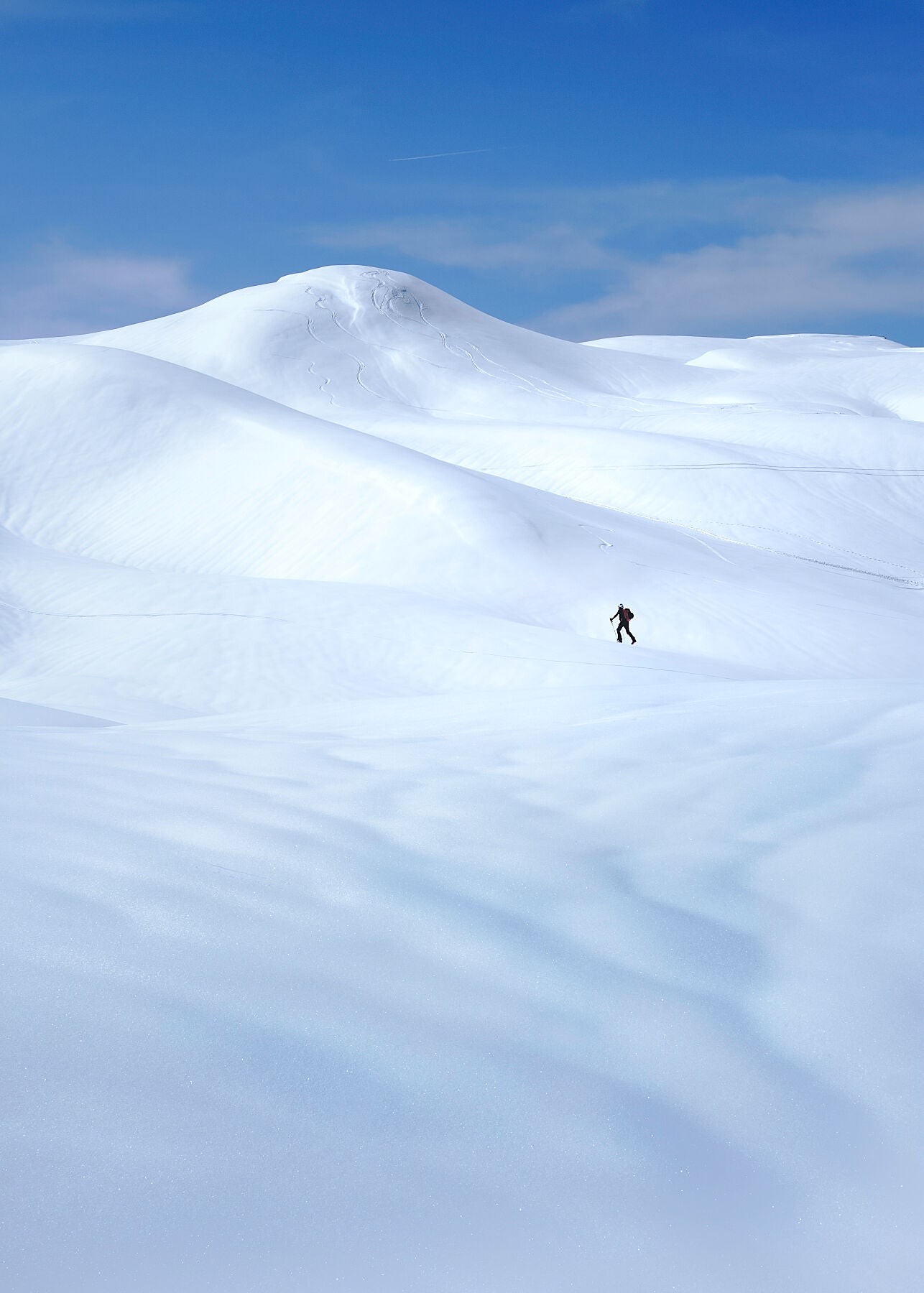 Minimilist photo of a ski tourer near Chamonix Mont Blanc in a field of snow with beautiful contours and blue sky