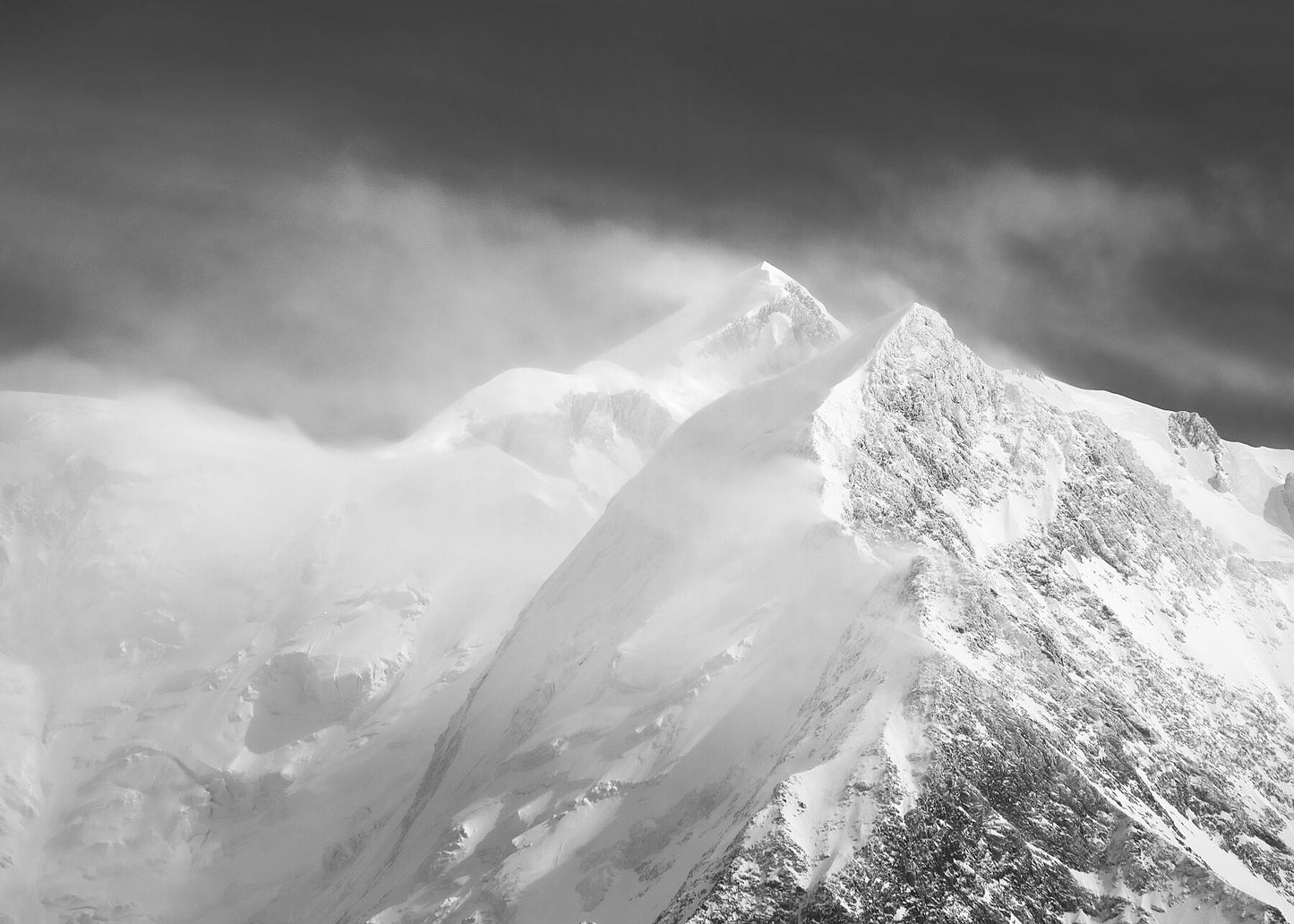 This black and white photograph captures view towards the summit of Mont Blanc in the French alps during a violent wind that snatches snow from the peaks and creates the illusion of the mountain steaming.