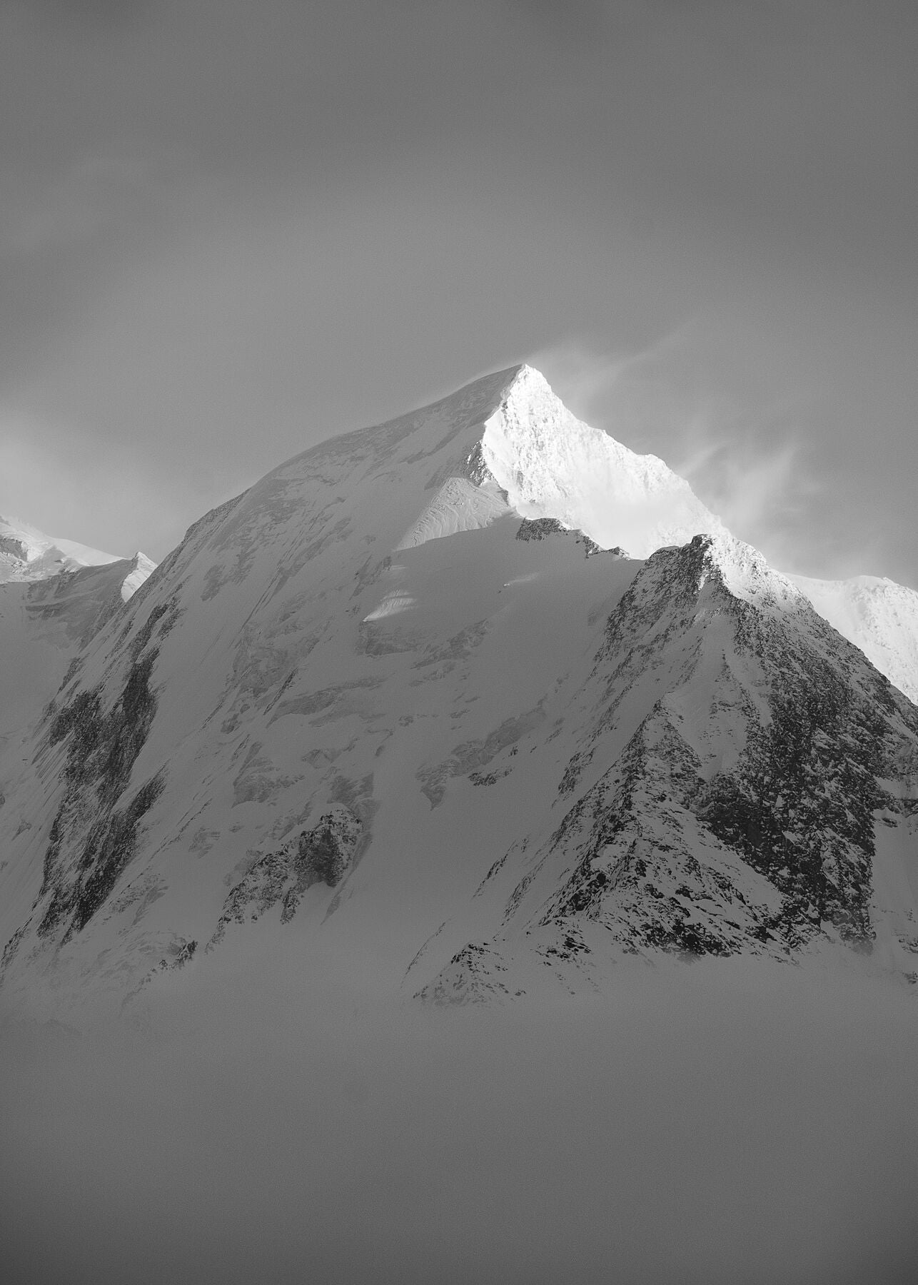 black and white photograph captures the strong wind blowing snow off the summit of the Aiguille de Bionnassay high in the French alps