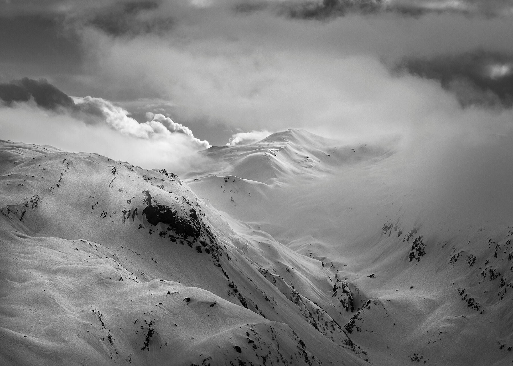 Black and white landscape photo of snowy mountains with swirling clouds