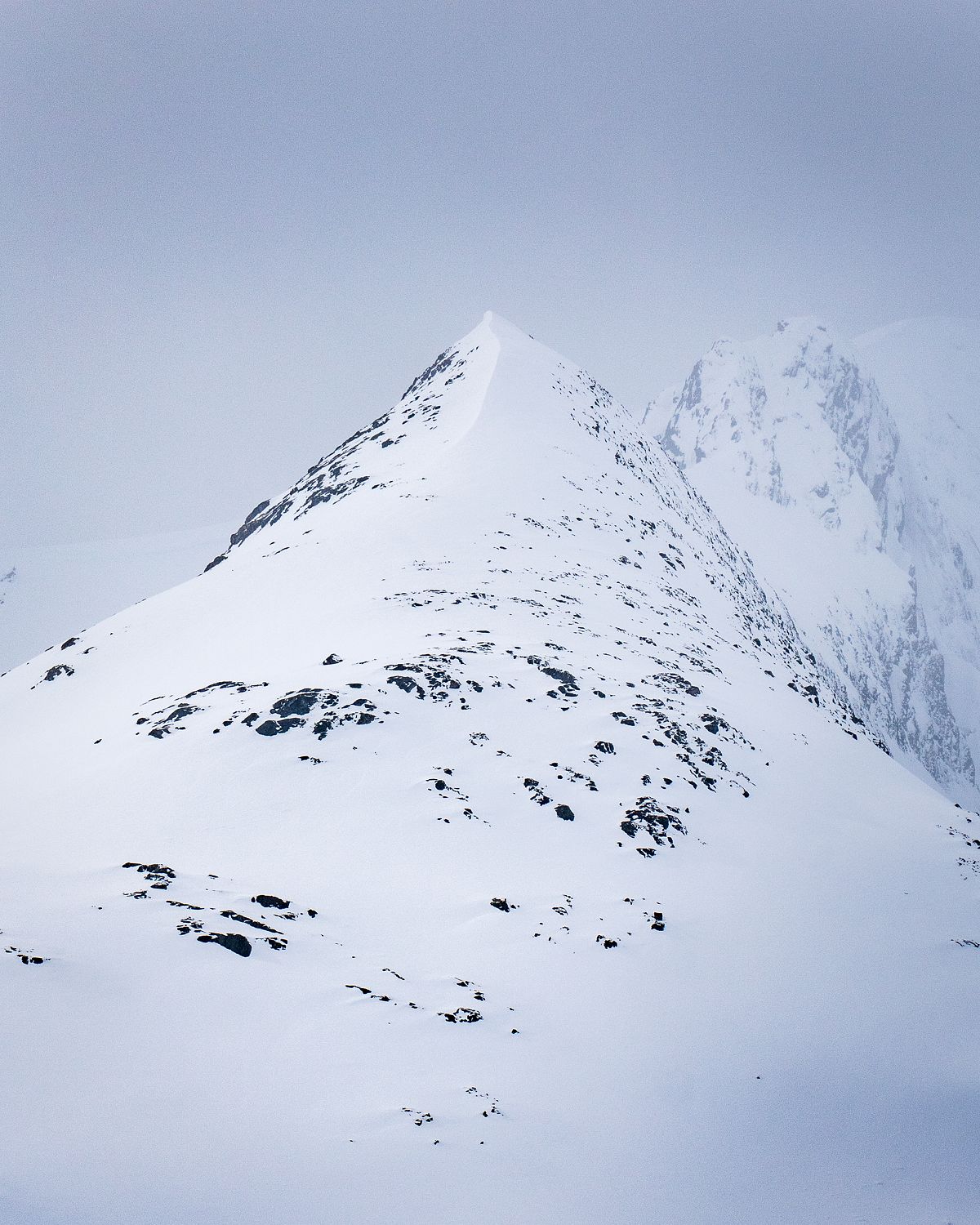 Two snow covered Norwegian mountain peaks emerge through soft light and mist