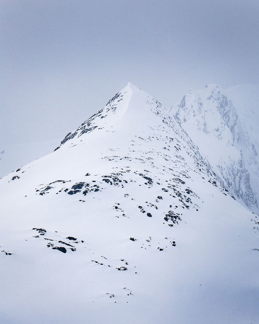 Two snow covered Norwegian mountain peaks emerge through soft light and mist